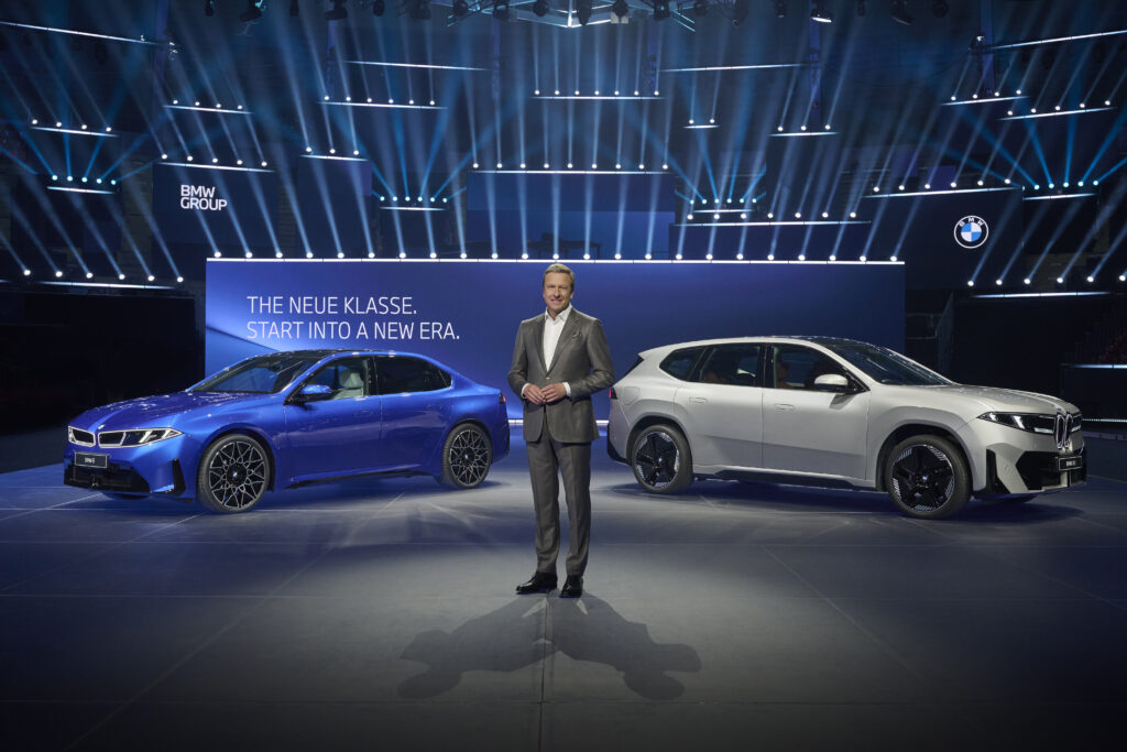 mann-im-anzug-steht-zwischen-blauem-und-grauem-bmw